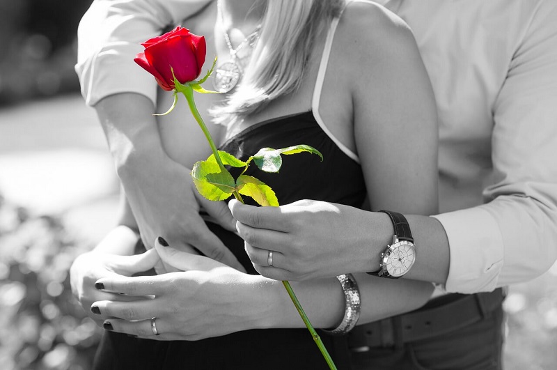 後ろから抱きしめる男性と、手に持った1本の赤いバラ
